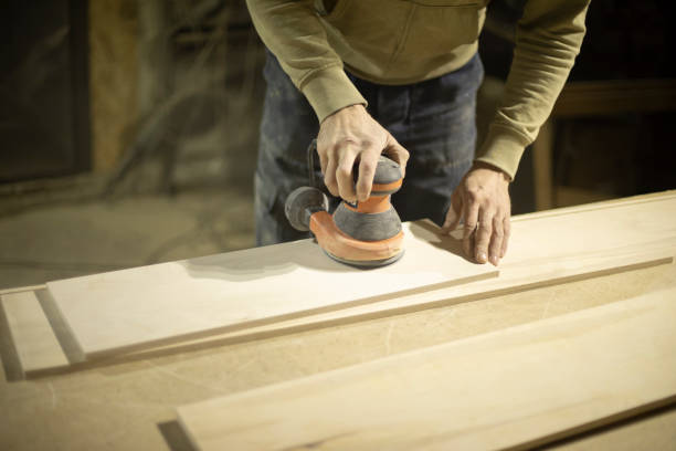 istock Carpenter grinds wood. Grinding tool. Guy in workshop handles board. 1372860579