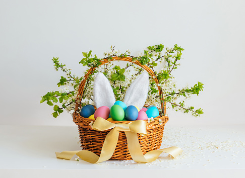 Easter basket with eggs and bunny ears on a white background. Beautiful Easter composition. Festive decor.