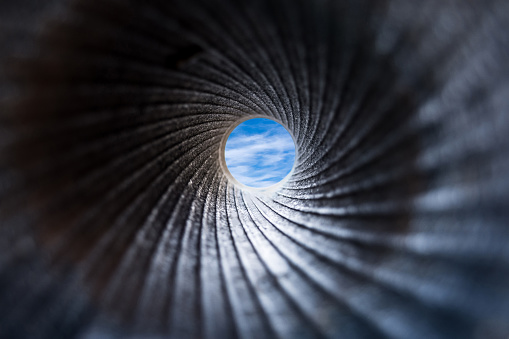 A view through a dark barrel of cannon to the blue sky with white fluffy clouds. Close up, selective focus. Abstract background concept
