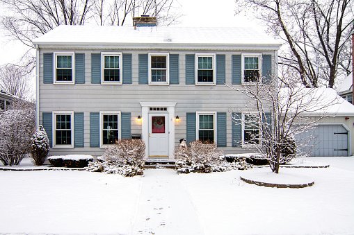 Traditional brick two story house with snow covered front yard in winter