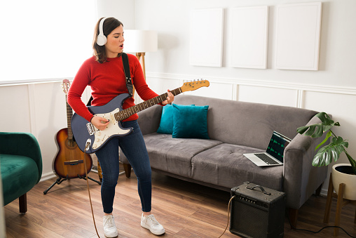 Passionate young woman singing a song while playing the electric guitar connected on an amplifier