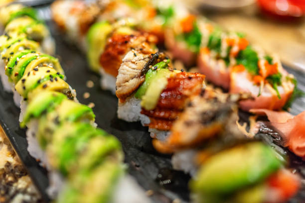 sushi rolls at restaurant. luxury sushis with avocado and eel topping, rainbow maki, tuna, tobiko, sesame seeds. japanese food. - sushischotel stockfoto's en -beelden