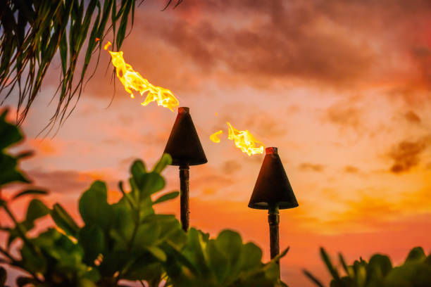 Hawaii luau party Maui fire tiki torches with open flames burning at sunset sky clouds at night. Hawaiian cultural travel vacation background. stock photo