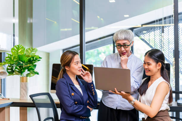 Senior businesswoman team leader is guiding young member to business success by showing information in laptop computer for goal achievement for startup and creativity project concept Senior businesswoman team leader is guiding young member to business success by showing information in laptop computer for goal achievement for startup and creativity project teacher retirement party stock pictures, royalty-free photos & images