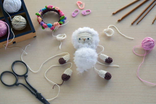 Making fanny sheep with wreath of flowers. Crochet toy ewe for child. On the table threads, needles, hook, cotton yarn. Step 1 - knit all details of toy. Handmade crafts. DIY concept. Small business. Income from hobby haciendo ovejas riñoneras con corona de flores. oveja de juguete de ganchillo para niño. en la mesa hilos, agujas, gancho, hilo de algodón. paso 1 - teje todos los detalles del juguete. artesanía artesanal. concepto diy. pequeña empresa. ingresos por