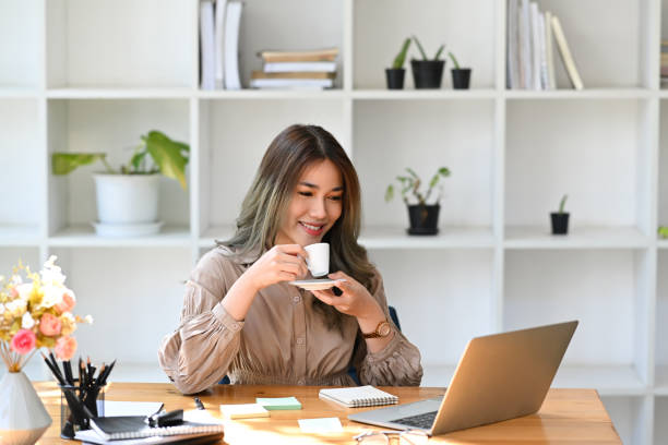 istock Relaxed beautiful businesswoman drinking coffee and reading email on her laptop computer. 1372904804