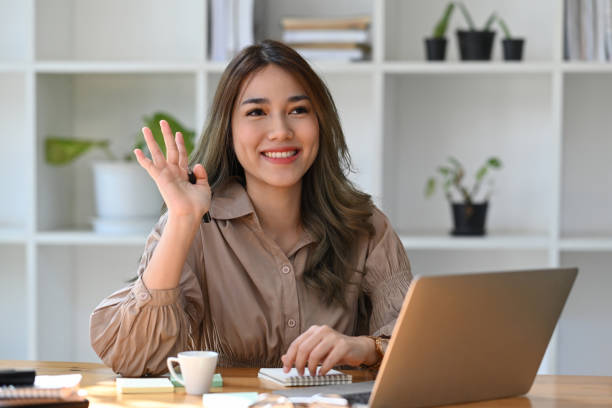 istock Friendly asian woman office worker greeting colleagues while working with computer laptop. 1372904821
