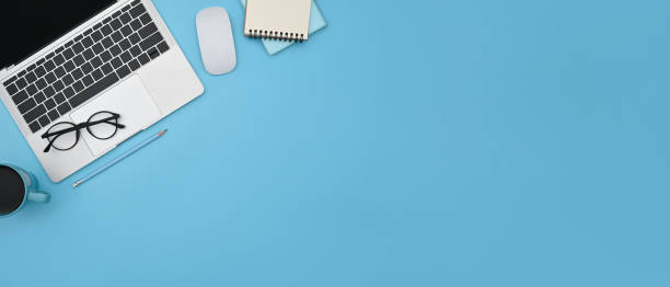 istock Computer laptop, notepad, eyeglasses and coffee cup on blue background with copy space. 1372905351