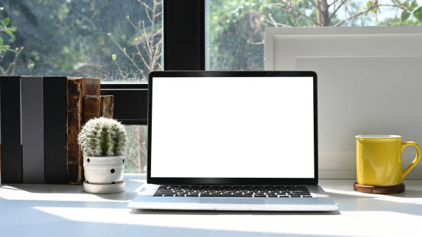 istock Mockup laptop computer, picture frame, books and cactus on white table in bright home office. 1372905373