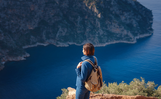 Butterfly Valley (kelebekler vadisi) in city of Oludeniz Fethiye in western Turkey. You can only reach this valley by boat or rock climbing. woman looks down on sea from cliff.