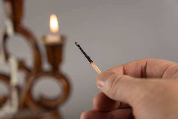 istock A man's hand holds an extinguished match against the burning candles. Brown ceramic candlestick in the background. Gray background. Closeup. Selective focus. 1372920503