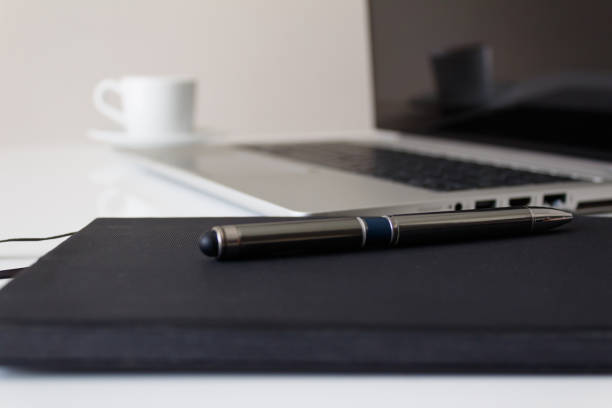 The concept of a workplace with a notebook with a pen, a laptop and coffee on a modern white office desk. Side view.