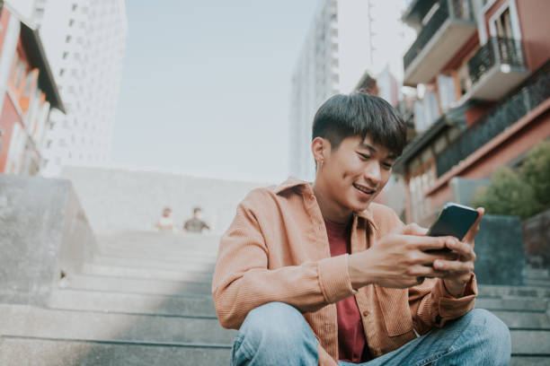 Asian male university student texting message on his mobile phone.