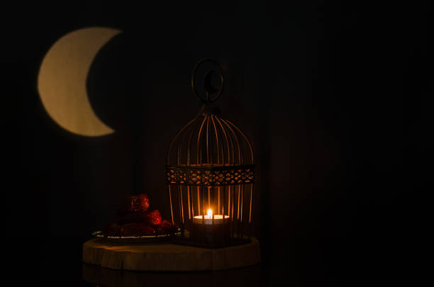 istock Lantern and small plate of dates fruit on wooden tray with moon shape from light on background 1372935908
