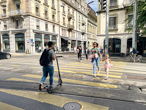 Geneva, Switzerland - September 15 2021: a mother gives her daughter in pink ballerina dress a hand while crossing the street in the busy city