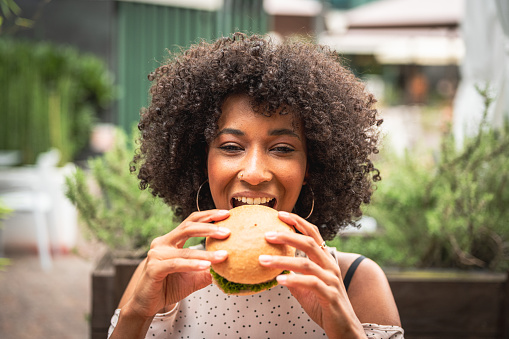 young african woman enjoying eating veggie burger at restaurant, healthy food and new concept of habits and feeding
