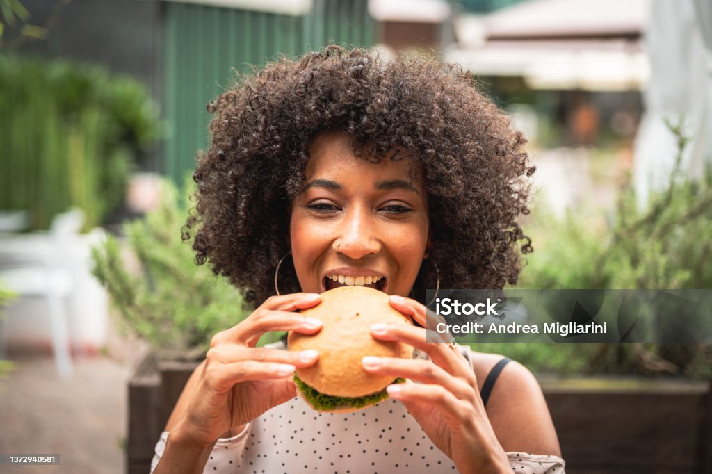 young african woman enjoying eating veggie burger at restaurant, healthy food and new concept of habits and feeding Eating Stock Photo