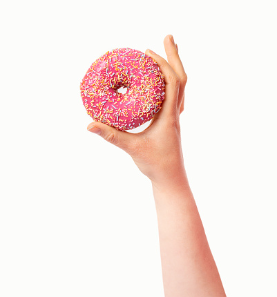 Female hand holding pink donut over white background. Top view, flat lay. Sweet, dessert, diet concept. Banner with copy space. Weight lost after holidays.