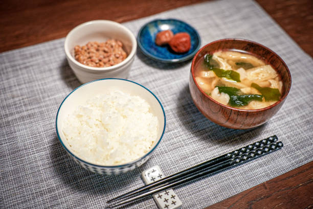 白米、味噌汁、納豆の発酵、梅干しの漬け梅干しをストライプグレーのテーブルクロスに入れた伝統的な日本のランチセットテイショク - 漬物 ストックフォトと画像