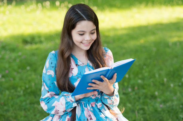 Child girl relaxing outdoors with book, excited about reading concept.