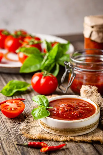 Bowl of italian tomato sauce with basil and fresh tomatoes on wooden background