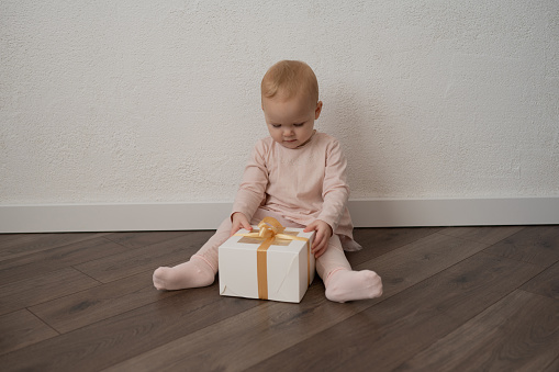 A little girl in pink clothes with a gift on a white wall background