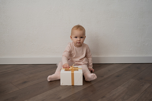 A little girl in pink clothes with a gift on a white wall background