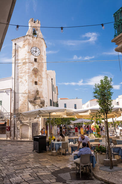 Characteristic square and tower clock with gazebo bar and people tourists in the center of Monopoli (Puglia) Monopoli, Italy - 20 August 2021: Characteristic square and tower clock with gazebo bar and people tourists in the center of Monopoli (Puglia) monopoli puglia stock pictures, royalty-free photos & images