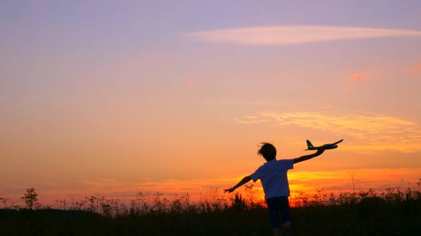 un garçon au coucher du soleil court à travers le champ dans ses mains un avion, le kid rêve de devenir pilote astronaute. rêve d’enfant de courir avec un jouet. pilote d’un avion pour enfants. concept de rêve - aspirations pilot child airplane photos et images de collection