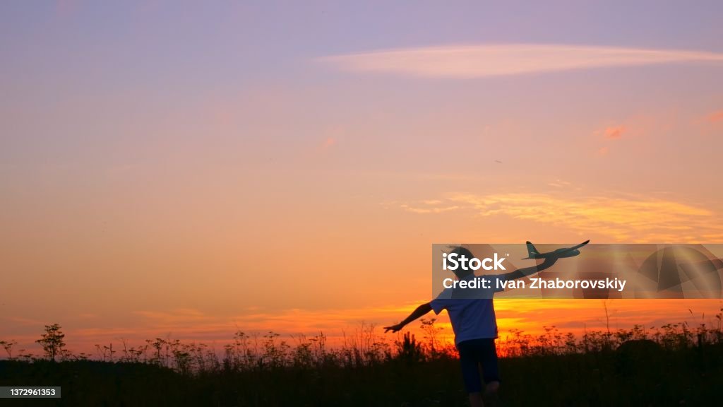 A boy at sunset runs across the field in his hands an airplane, the Kid dreams of becoming an astronaut pilot. Childhood dream to run with a toy. Pilot of a children's plane. Dream concept Airplane Stock Photo