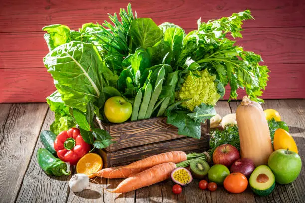 Photo of Assorted fruits and vegetables in a wooden box fresh after harvest on pink wall