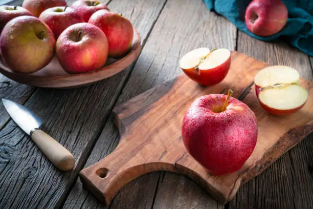 Red apple closeup wet with dew drops on cutting board and knife on wooden table plank, royal Gala apple