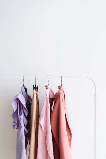 Capsule feminine cloth of pastel violet and pink color shades hanging on a rail over white background
