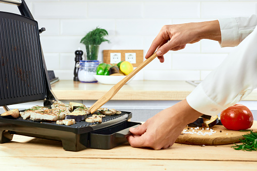 Woman holding spatula for cooking and serving barbecue on a table. Grill steak on an electric stove at kitchen.