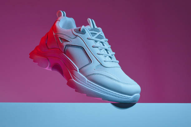 istock Modern white sneakers isolated over multicolor vivid purple neon light background. leather trainers on big sole with spikes. Bright colored photo. 1372970738