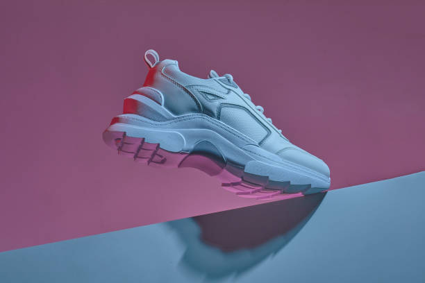 istock Modern white sneakers isolated over multicolor vivid purple neon light background. leather trainers on big sole with spikes. Bright colored photo. 1372970739