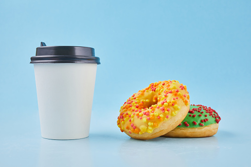 Sweet donut or doughnut with hot cup of fresh coffee or tea. Takeaway paper cup with donuts. Breakfast at the coffee shop concept.