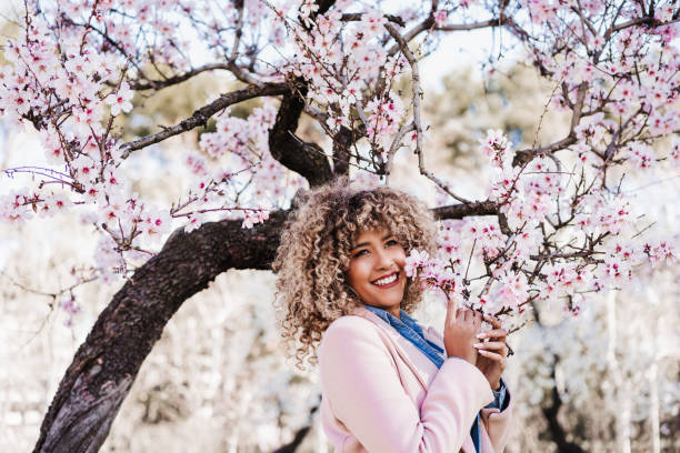 portrait of beautiful hispanic woman with afro hair in spring among pink blossom flowers. nature stock photo