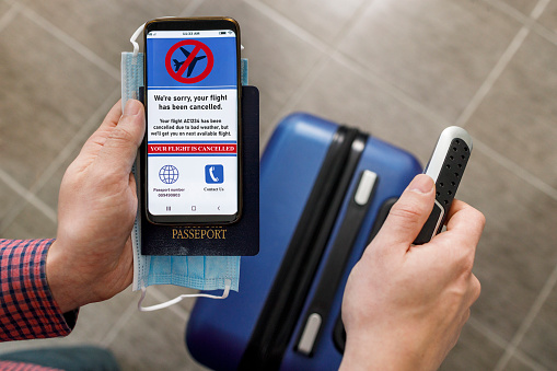 Traveler with a suitcase seeing on a smart phone that the flight was cancelled on