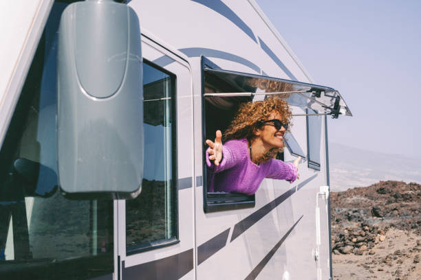Overjoyed and excited adult pretty woman admire outside the camper van window and outstretching arms with big smile. Concept of tourist people and tourism with rented vehicle. Nature campsite stock photo