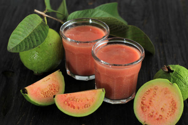 red guava juice is served on a wooden background with guava fruit slices and leaf decorations stock photo