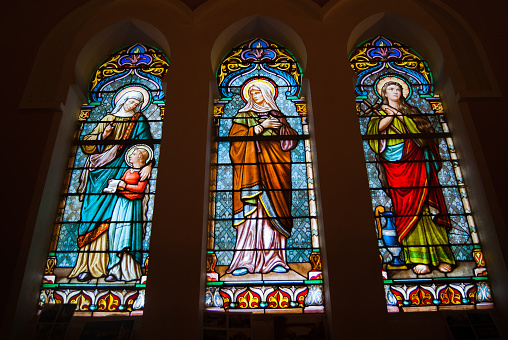 Medieval era rose window stained glass panels showing saints, angels set in stone gothic tracery in a cathedral.
