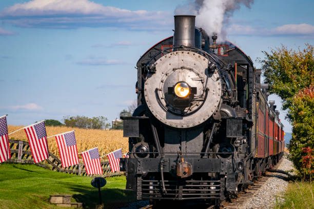 istock Antique Steam Engine Approach Thru Corn Fields With American Flags Lining the Track 1372980155