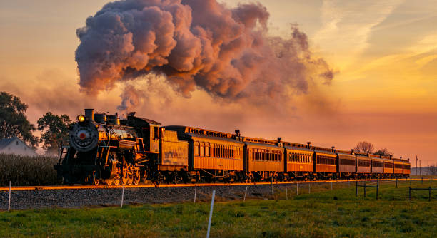 蒸気と煙の完全な頭で日の出に近づくアンティーク蒸気旅客列車の眺め - steam engine ストックフォトと画像