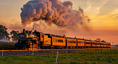 View of an Antique Steam Passenger Train Approaching at Sunrise With a Full Head of Steam and Smoke