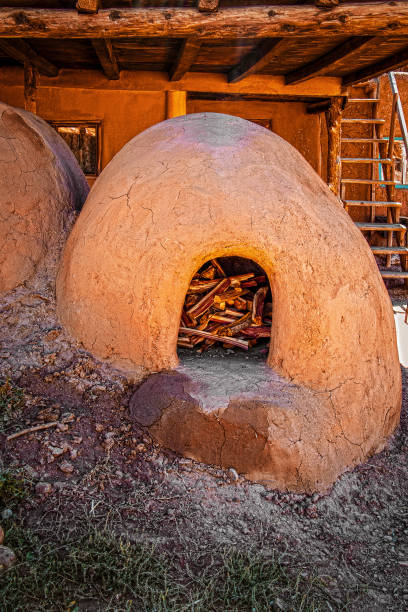 Horno, a mud adobe-built outdoor oven in Taos Pueblo New Mexico originally introduced to America by the Moors - filled with wood under a wooden overhang with stairs to second story of pueblo behind Horno, a mud adobe-built outdoor oven in Taos Pueblo New Mexico originally introduced to America by the Moors - filled with wood under a wooden overhang with stairs to second story of pueblo behind stove oven adobe outdoors stock pictures, royalty-free photos & images