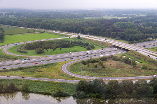 Top view of a highway intersection with car traffic and green fields and forests during day near 's-Hertogenbosch, the Netherlands, Europe