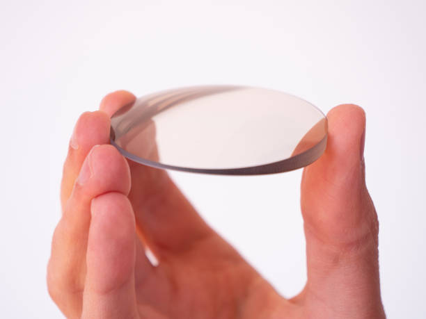 hand holds a circular lens of cut glass, lens cut for eyewear, production of clear lens for eyewear. - magnifying glass lens holding europe imagens e fotografias de stock