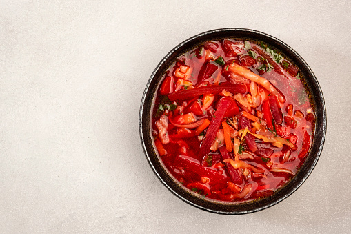 Homemade red cabbage soup with beets, vegetables and herbs, Russian borscht in plate on grey kitchen table background, top view, copy space. Vegan, vegetarian healthy diet local food