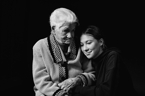 Elderly woman sitting with an adult granddaughter a black background. Black and white photo.